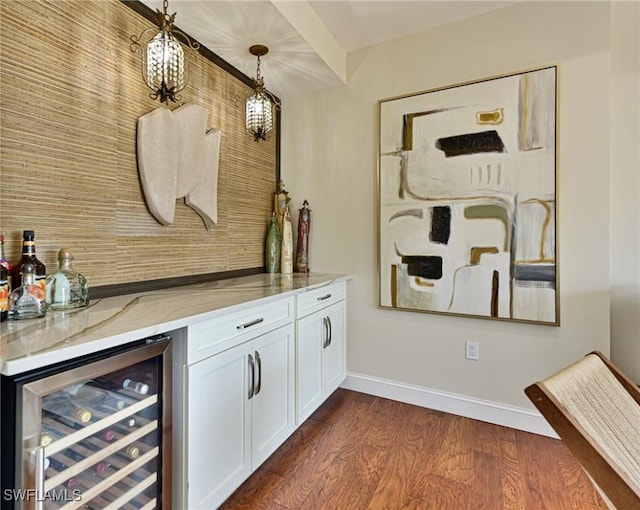 bar with dark wood-type flooring, light stone counters, decorative light fixtures, beverage cooler, and white cabinets