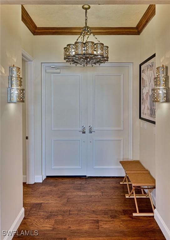 foyer entrance with an inviting chandelier, ornamental molding, and dark hardwood / wood-style floors