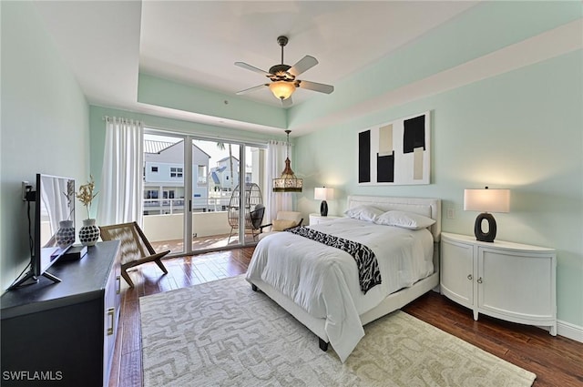 bedroom with dark hardwood / wood-style floors, ceiling fan, a tray ceiling, and access to exterior