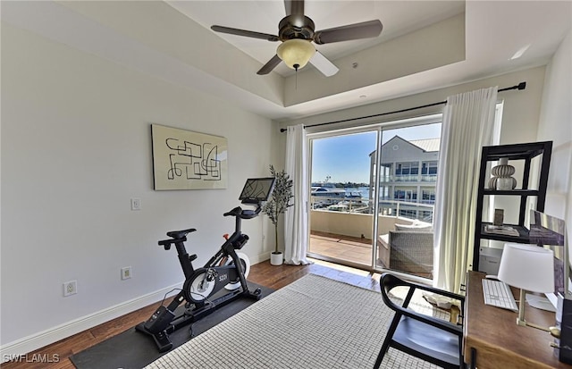 workout area with dark hardwood / wood-style floors, ceiling fan, and a tray ceiling