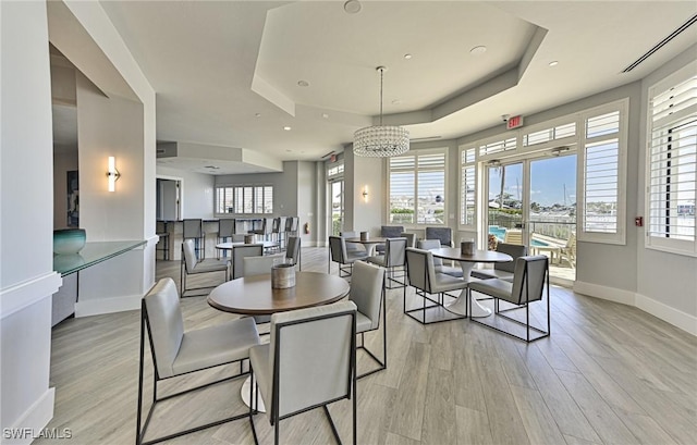 dining area with a healthy amount of sunlight, light wood-type flooring, and a tray ceiling