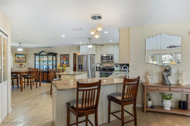 kitchen featuring a kitchen bar, sink, appliances with stainless steel finishes, kitchen peninsula, and pendant lighting