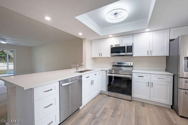 kitchen with appliances with stainless steel finishes, sink, white cabinets, kitchen peninsula, and a raised ceiling