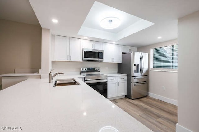 kitchen featuring sink, appliances with stainless steel finishes, white cabinetry, light hardwood / wood-style floors, and a raised ceiling