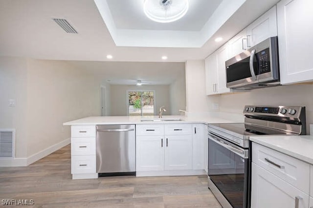 kitchen with sink, stainless steel appliances, kitchen peninsula, white cabinets, and a raised ceiling