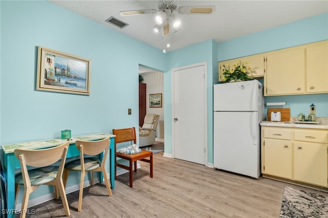 kitchen featuring white refrigerator, cream cabinets, light hardwood / wood-style floors, and a textured ceiling