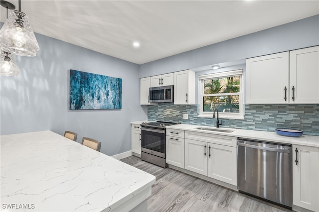 kitchen with decorative light fixtures, sink, white cabinets, backsplash, and stainless steel appliances