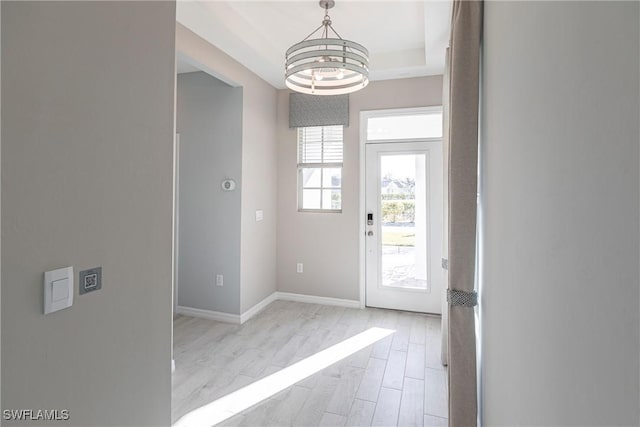 foyer with a notable chandelier, light hardwood / wood-style floors, and a raised ceiling