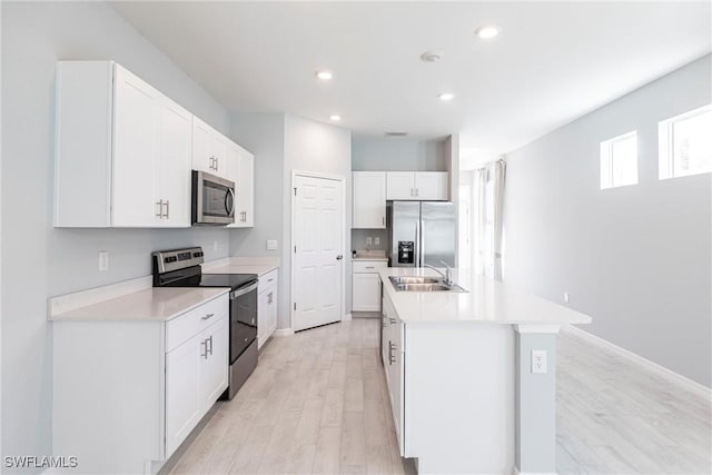 kitchen with appliances with stainless steel finishes, white cabinetry, sink, a center island with sink, and light wood-type flooring