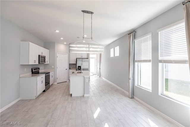 kitchen featuring pendant lighting, appliances with stainless steel finishes, white cabinetry, a kitchen island with sink, and light wood-type flooring