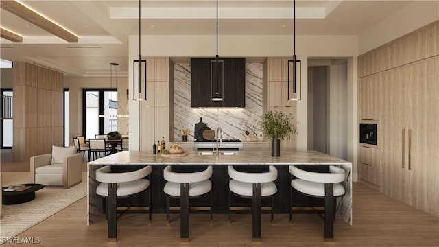 kitchen with pendant lighting, a breakfast bar area, a kitchen island with sink, light stone counters, and light hardwood / wood-style flooring