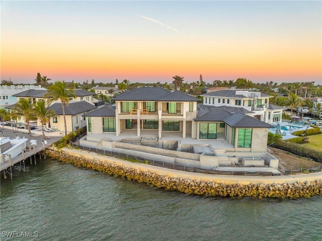 back house at dusk featuring an outdoor hangout area, a patio area, a balcony, and a water view