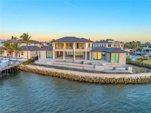 back house at dusk with a water view, a balcony, and a patio