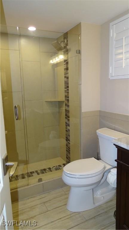 bathroom with a shower with door, vanity, tile walls, and toilet