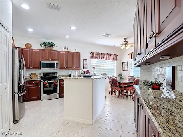 kitchen featuring light tile patterned floors, ceiling fan, appliances with stainless steel finishes, backsplash, and light stone countertops