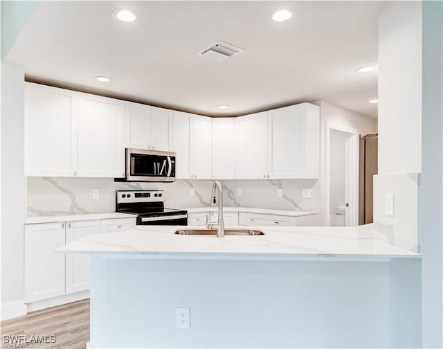 kitchen featuring sink, appliances with stainless steel finishes, white cabinetry, light stone counters, and kitchen peninsula