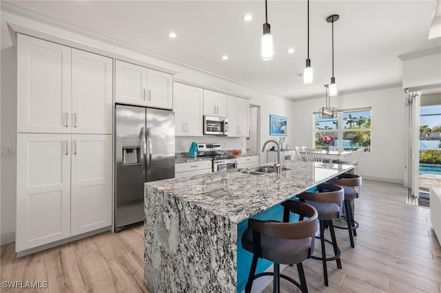 kitchen featuring sink, white cabinetry, stainless steel appliances, an island with sink, and decorative light fixtures