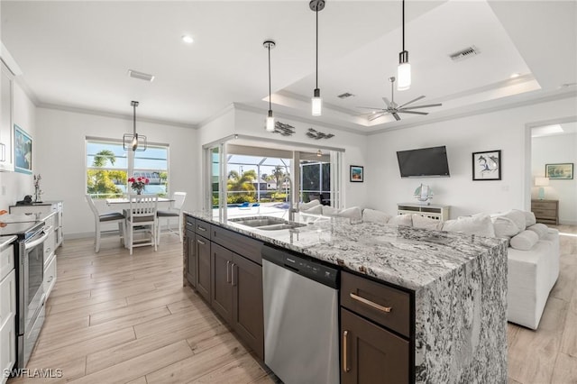 kitchen featuring appliances with stainless steel finishes, decorative light fixtures, a raised ceiling, and a kitchen island with sink