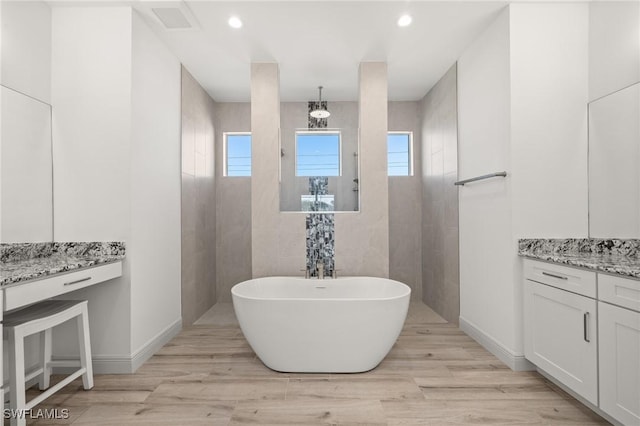 bathroom with a tub to relax in, a healthy amount of sunlight, vanity, and hardwood / wood-style floors