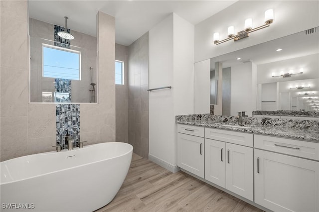 bathroom with hardwood / wood-style flooring, vanity, a bathing tub, and tile walls