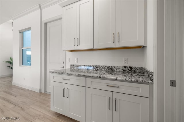 bar featuring white cabinetry, ornamental molding, light stone counters, and light hardwood / wood-style flooring