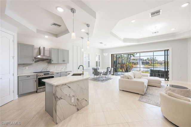 kitchen featuring stainless steel electric stove, a raised ceiling, light stone countertops, and wall chimney range hood