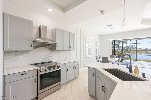 kitchen with wall chimney exhaust hood, sink, gray cabinetry, stainless steel electric range oven, and hanging light fixtures