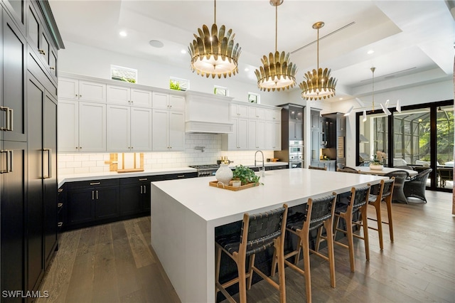 kitchen with a tray ceiling, plenty of natural light, decorative light fixtures, and a large island with sink