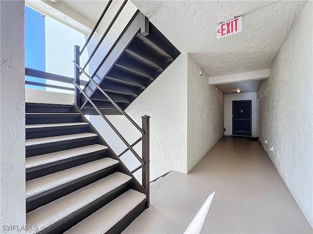 stairway with a textured ceiling and concrete floors