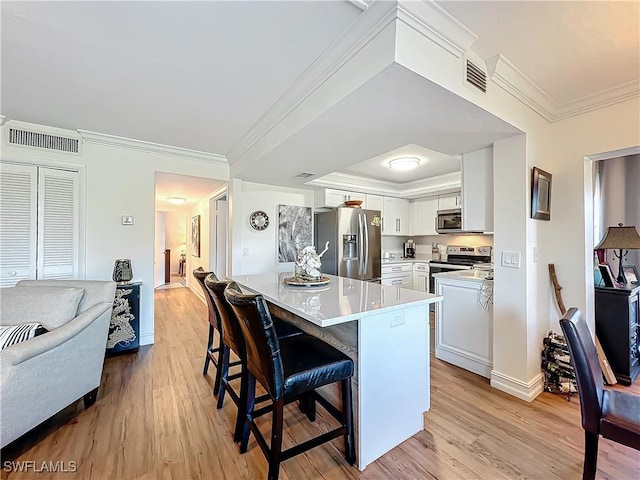 kitchen with appliances with stainless steel finishes, white cabinets, a kitchen breakfast bar, kitchen peninsula, and light hardwood / wood-style flooring