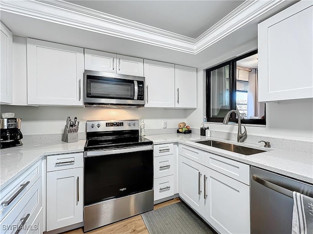 kitchen with appliances with stainless steel finishes, white cabinetry, sink, light stone counters, and crown molding