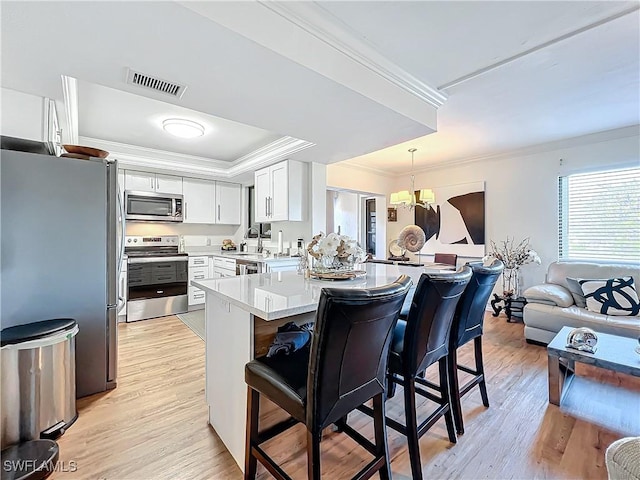 kitchen featuring pendant lighting, crown molding, a breakfast bar, white cabinetry, and stainless steel appliances