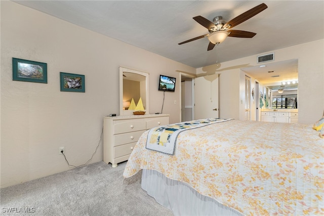 bedroom with ceiling fan, light colored carpet, and ensuite bath