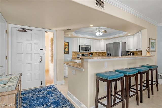 kitchen featuring a breakfast bar, white cabinetry, ornamental molding, appliances with stainless steel finishes, and kitchen peninsula