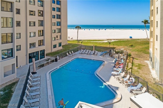 view of swimming pool featuring a patio, a water view, and a beach view