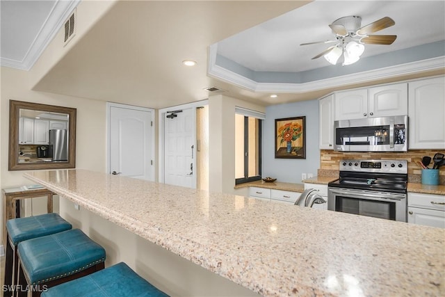 kitchen with stainless steel appliances, crown molding, white cabinets, and a kitchen breakfast bar