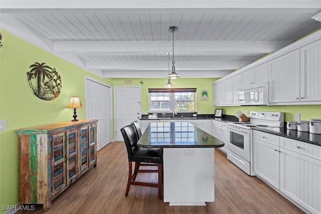 kitchen with white appliances, a breakfast bar, white cabinetry, a kitchen island, and decorative light fixtures