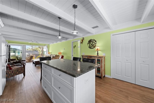 kitchen featuring pendant lighting, wood-type flooring, dark stone countertops, white cabinets, and a center island