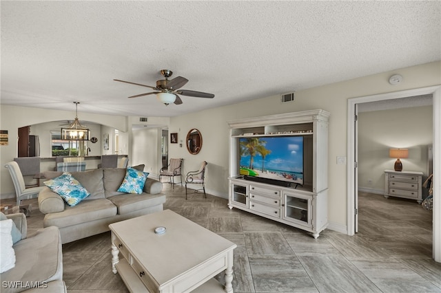 living room with ceiling fan with notable chandelier and a textured ceiling