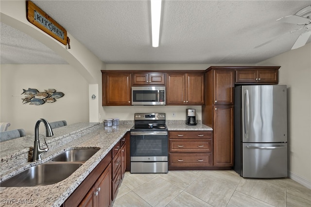 kitchen with sink, a textured ceiling, ceiling fan, stainless steel appliances, and light stone countertops