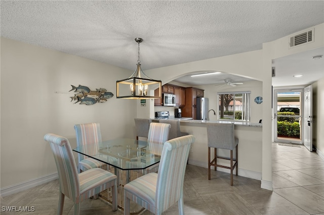 dining area featuring light tile patterned flooring, sink, ceiling fan with notable chandelier, and a textured ceiling