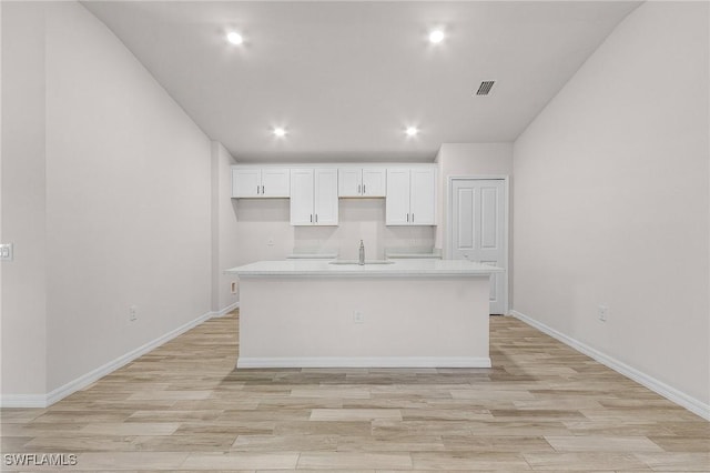 kitchen with light wood-type flooring, sink, a kitchen island with sink, and white cabinets