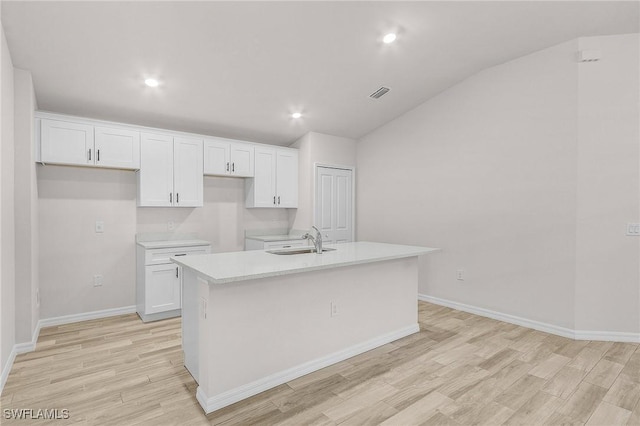 kitchen with white cabinetry, an island with sink, vaulted ceiling, and light hardwood / wood-style floors