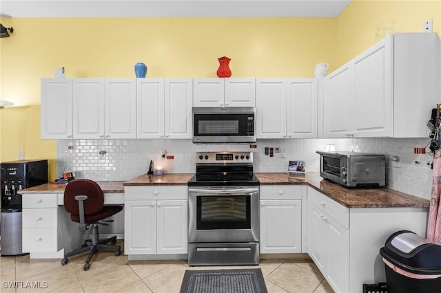 kitchen with appliances with stainless steel finishes, white cabinetry, backsplash, dark stone counters, and light tile patterned floors