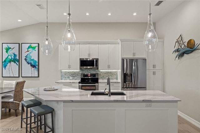 kitchen with appliances with stainless steel finishes, sink, white cabinets, a kitchen island with sink, and light stone counters