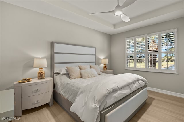 bedroom with a raised ceiling, ceiling fan, and light hardwood / wood-style floors