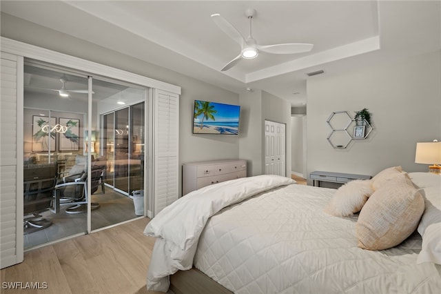 bedroom with ceiling fan, hardwood / wood-style floors, a tray ceiling, access to outside, and a closet