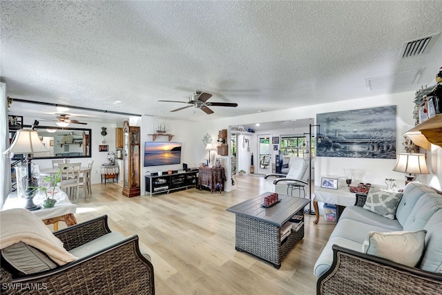 living room featuring ceiling fan, light hardwood / wood-style flooring, and a textured ceiling