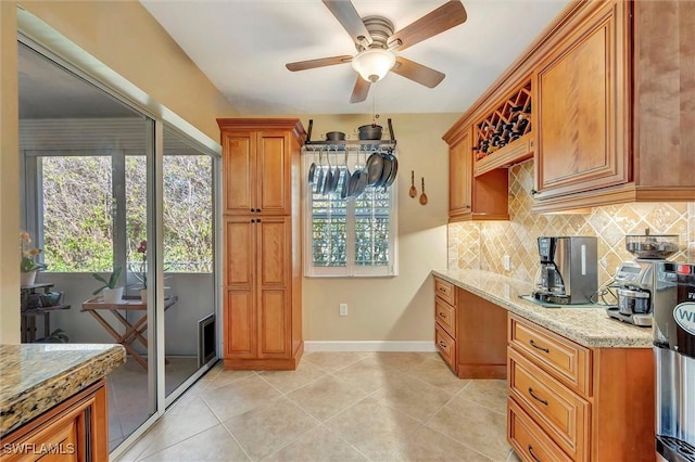 kitchen with built in desk, tasteful backsplash, light tile patterned floors, ceiling fan, and light stone counters