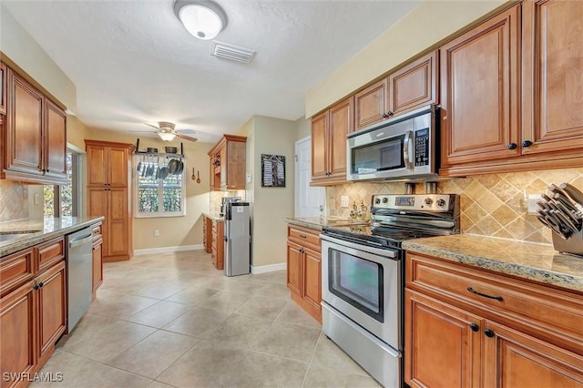 715 96th Ave N, Naples, FL 34108 - kitchen with stainless steel appliances, brown cabinetry, baseboards, and light stone counters